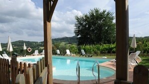 A pool area with lounge chairs and umbrellas, surrounded by a wooden fence, and a view of the countryside. - Agriturismo Podere Casenove (Citerna)