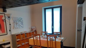 A dining area with a table set for two, wooden chairs, a bookshelf, and a window with curtains. - Romeo and Juliet B&B and Apartaments (Bergamo)