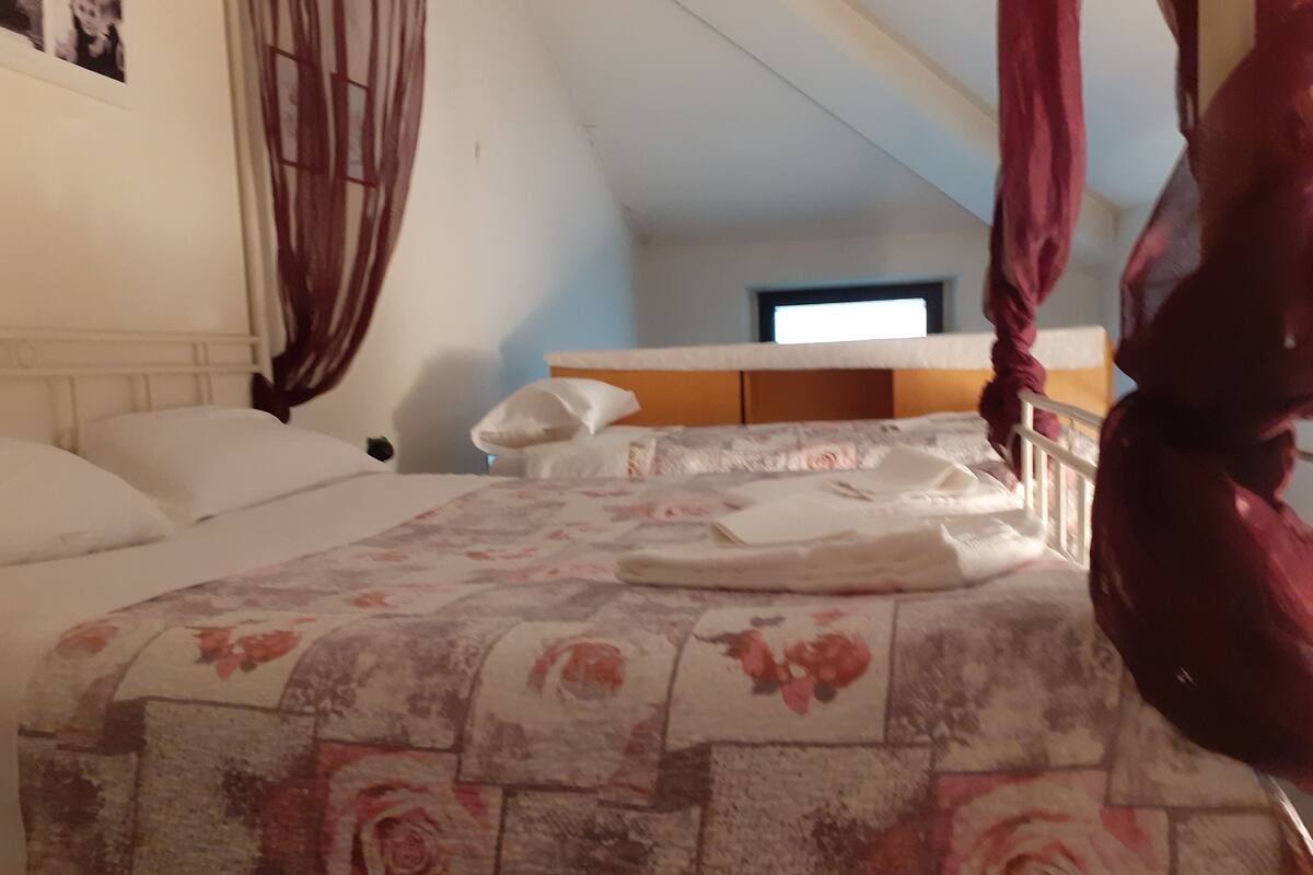 A bedroom with a bed, a nightstand, a window, and a curtain.