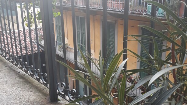 A balcony with a wrought iron railing, potted plants, and a building with green shutters in the background. - Romeo and Juliet B&B and Apartaments (Bergamo)