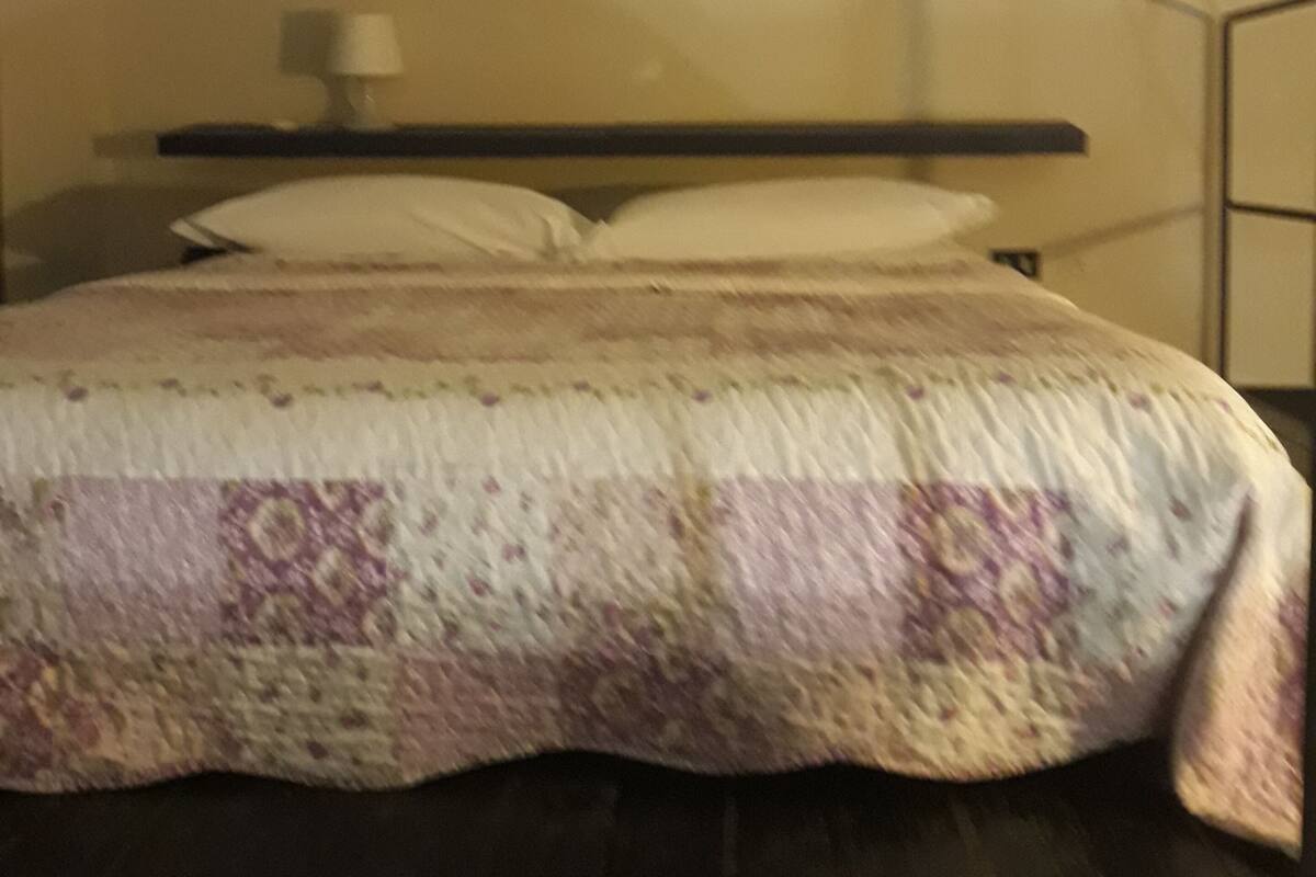 A bed with a patterned bedspread, a bedside lamp, and a wall-mounted picture.