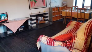 A living room with a sofa, a TV, a fireplace, a bookshelf, and a dining area with chairs and a table. - Romeo and Juliet B&B and Apartaments (Bergamo)