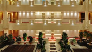 Eine mehrstöckige Hotelhalle mit einem zentralen Atrium, mehreren Etagen und zahlreichen Blumentöpfen.