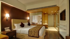Ein Hotelzimmer mit einem großen Bett, Nachttischen, einem Schreibtisch, einem Spiegel und einem Fernseher.