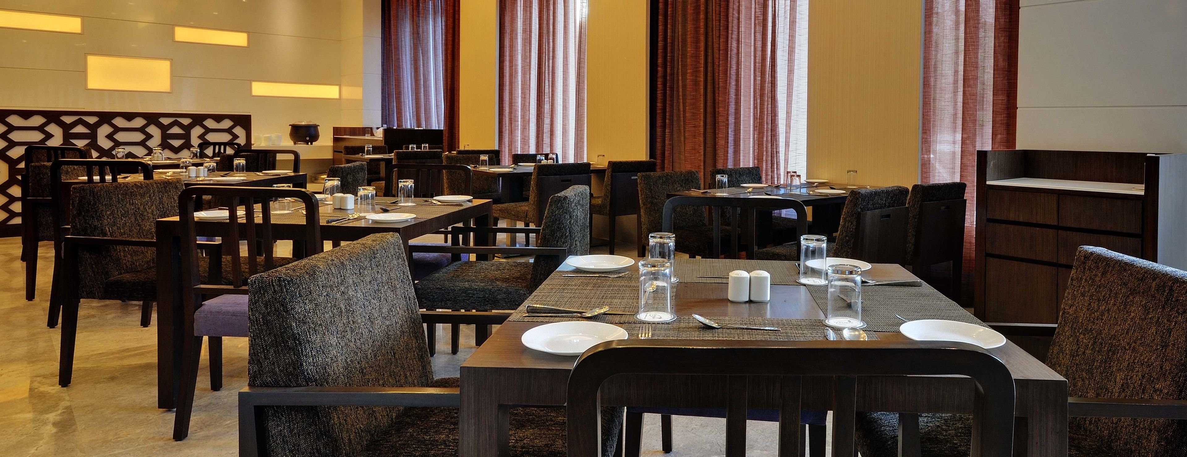 A hotel dining area with multiple tables set for guests, equipped with plates, glasses, and cutlery.