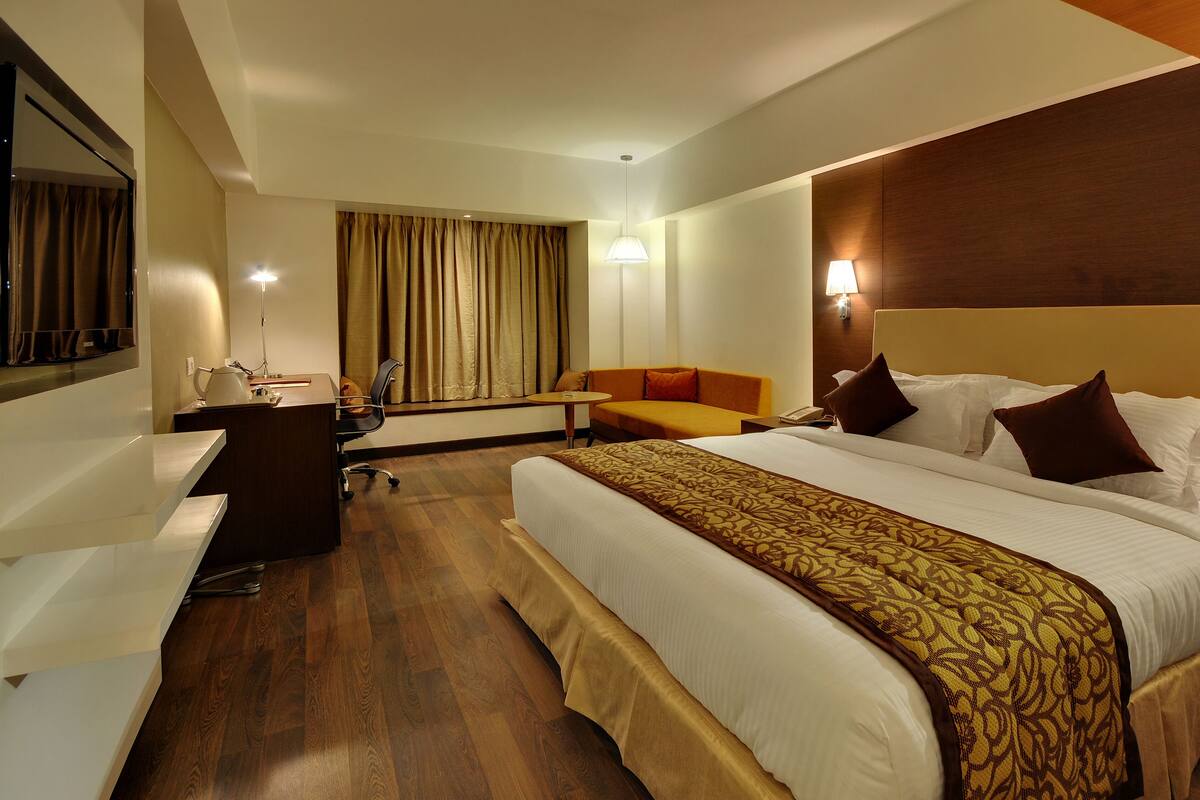 A hotel room with a large bed, a desk, a chair, a sofa, and a small table.
