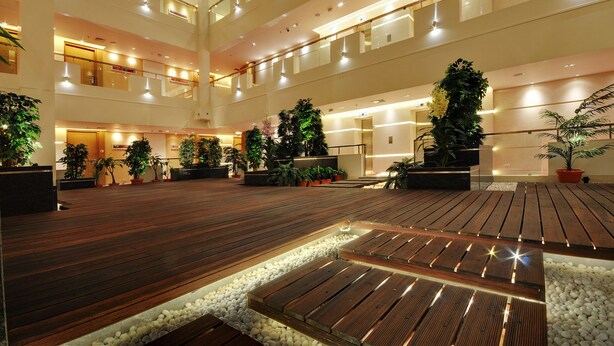 Ein mehrgeschossiges Atrium mit Holzböden, Topfpflanzen und moderner Beleuchtung.
