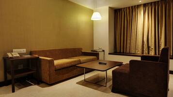 A hotel room with a sofa, a small table, a chair, a lamp, and a window with curtains.