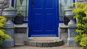 A stone building with a blue door, a window above the door, and two planters with plants. - Church View B&B (Gurteen)