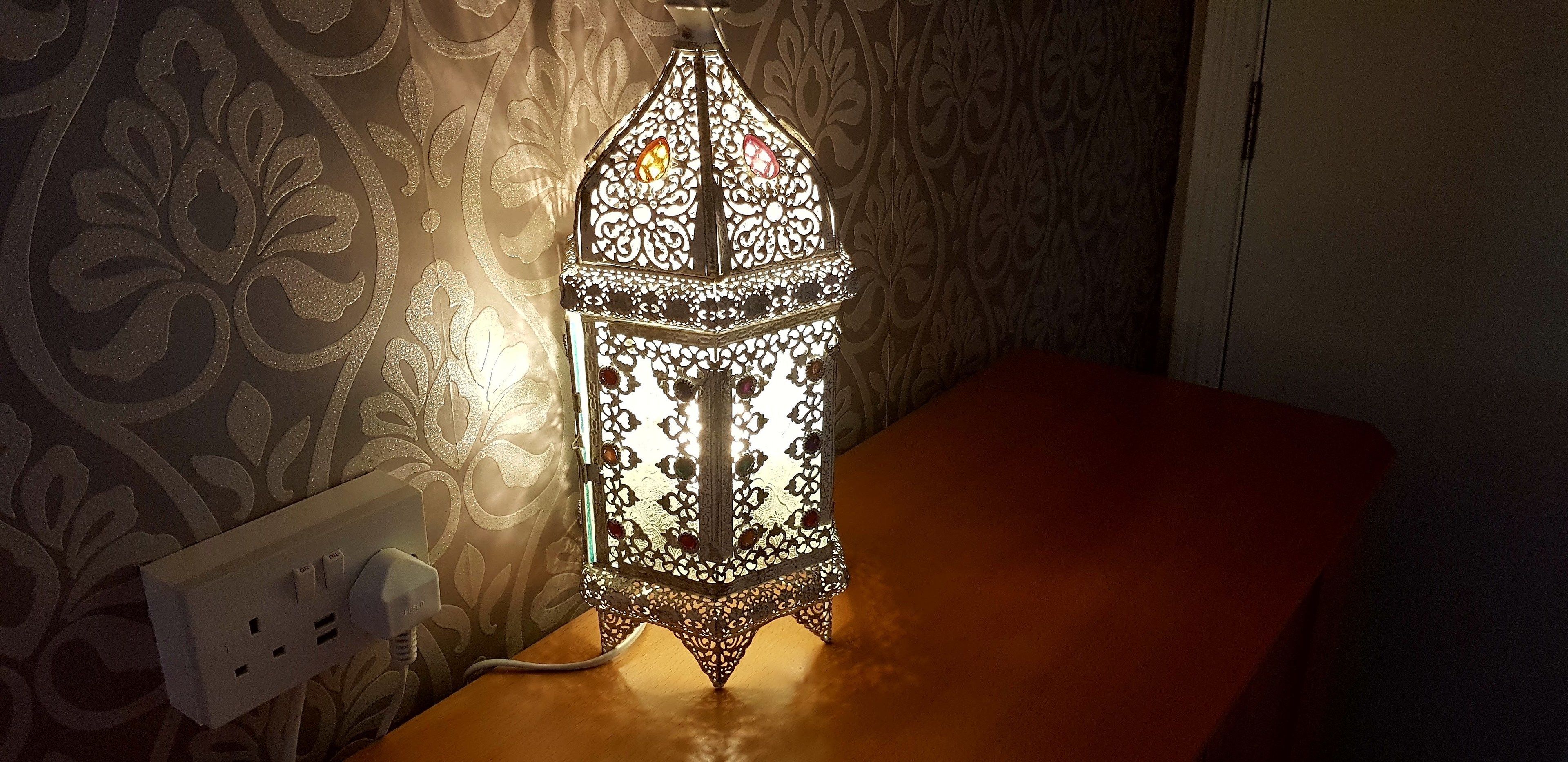 Un farol decorativo sobre una mesa de madera, con un fondo de papel tapiz estampado.