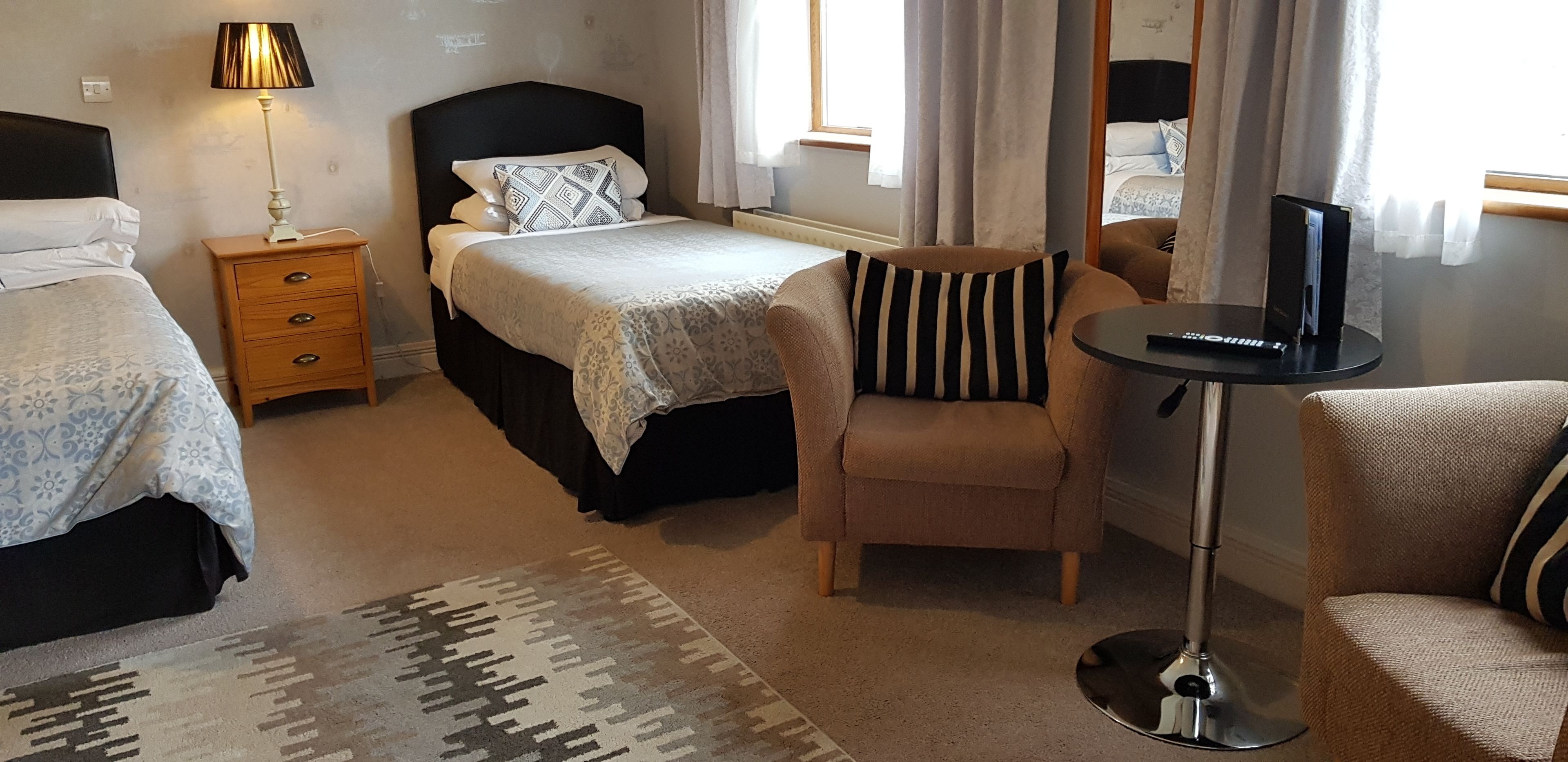 A hotel room with two beds, a chair, a small table with a lamp, and a TV.
