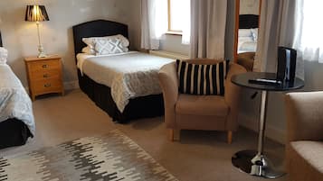 A hotel room with two beds, a chair, a small table with a lamp, and a TV.