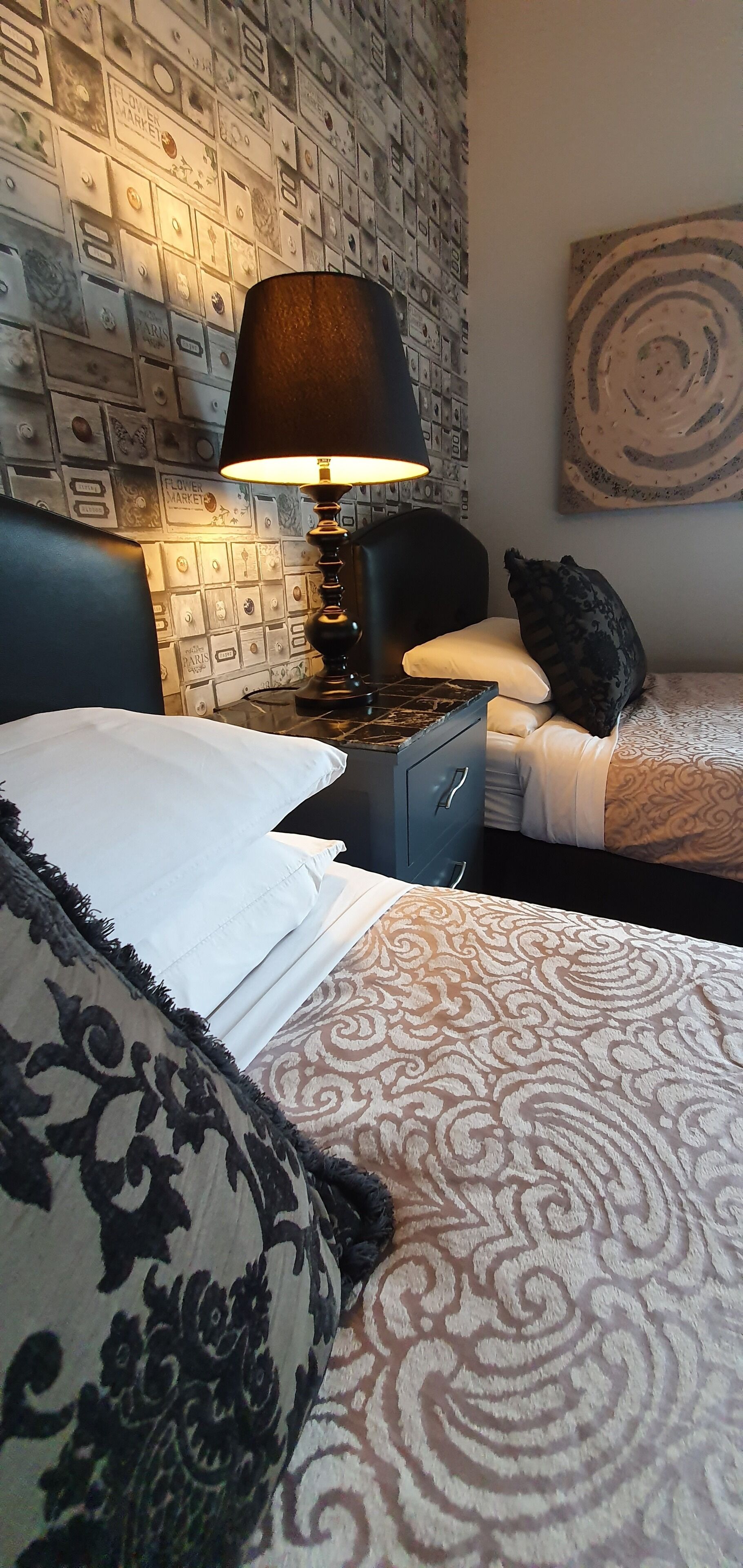 Habitación de hotel con pared estampada, cama con colcha estampada, mesita de noche con lámpara y una obra de arte colgada en la pared.