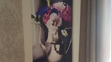 Fotografía en la pared de un jarrón con flores, un jarrón rojo y una silla gris.