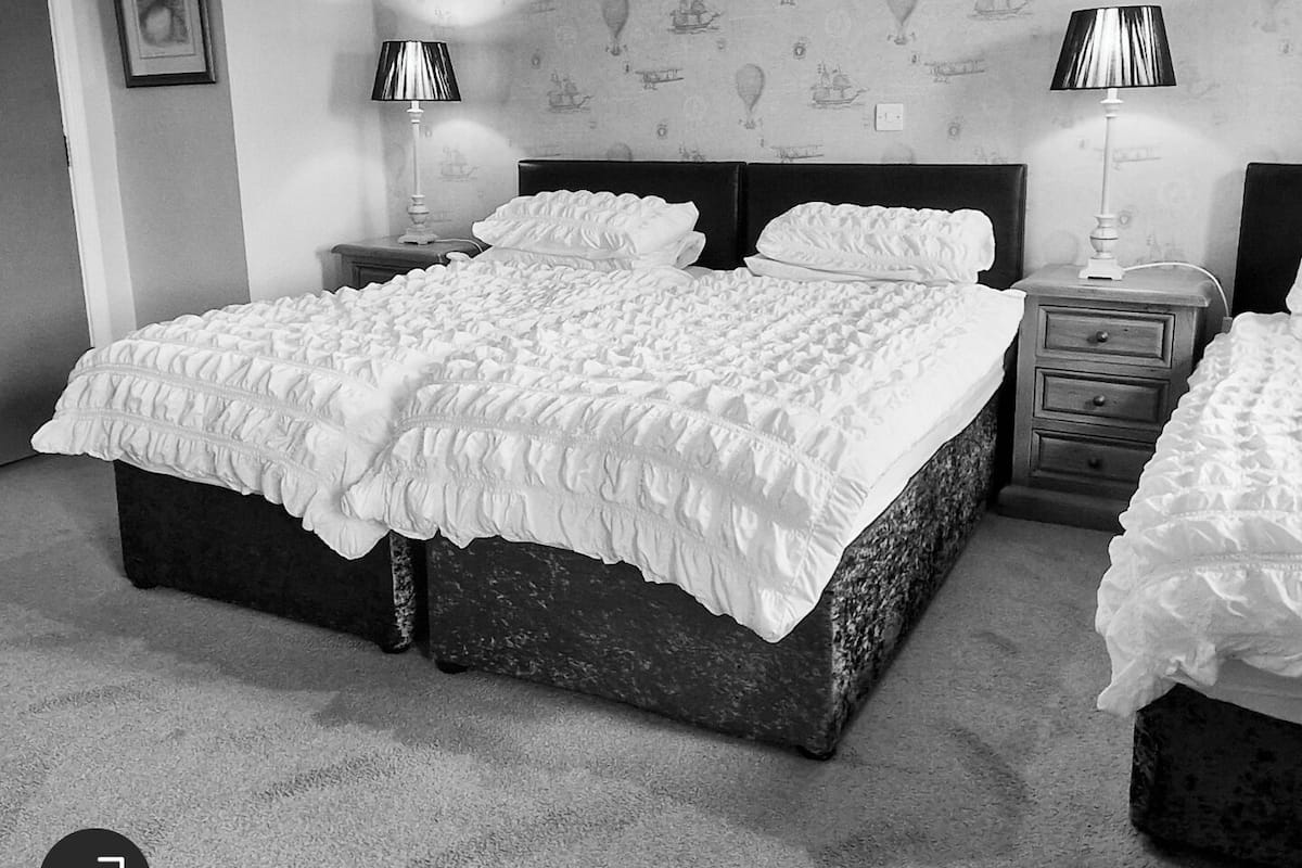 Quarto com uma cama grande, duas mesas de cabeceira com abajures, uma cômoda e um papel de parede estampado.