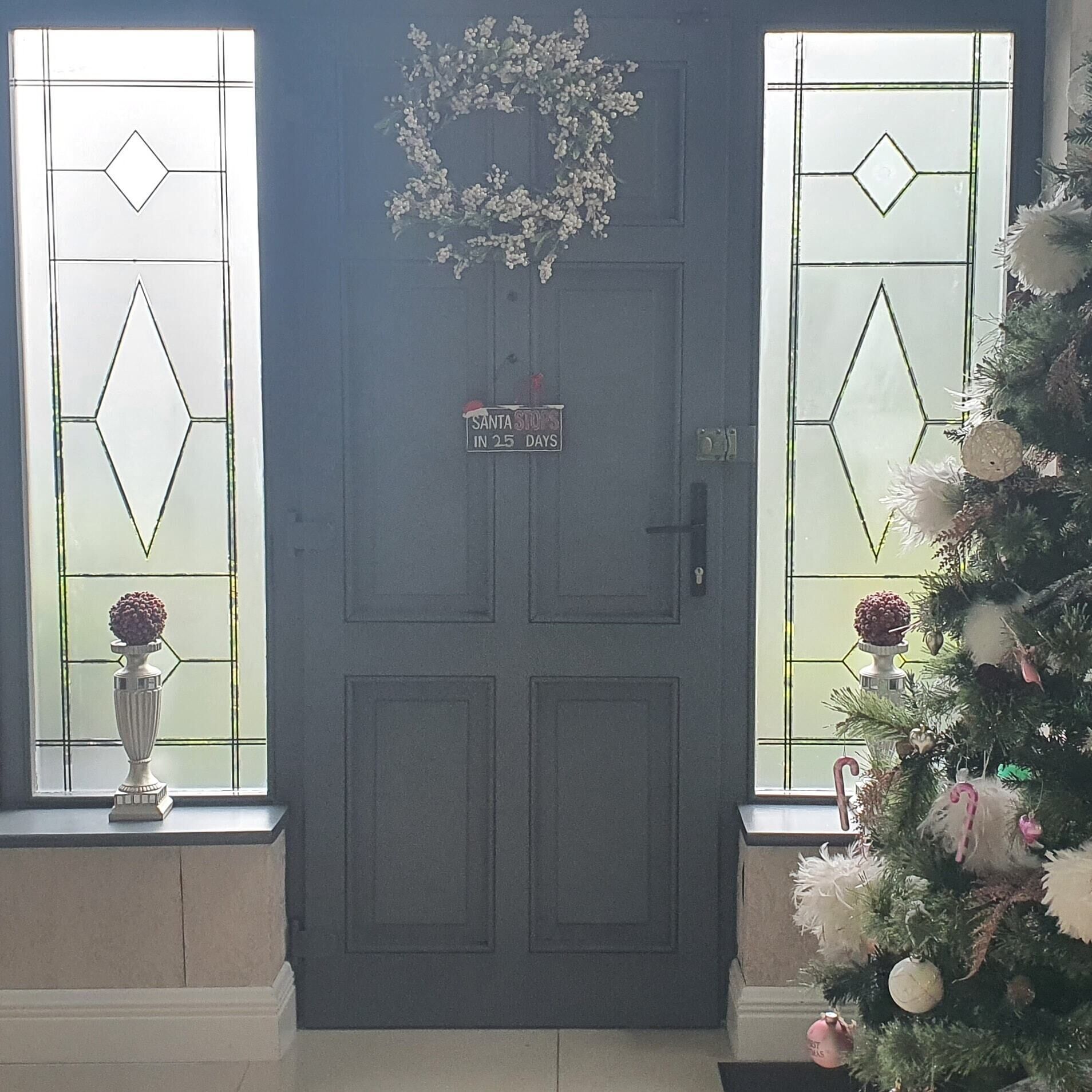 Una puerta azul con un adorno de laurel y un cartel que dice 'SANTA LLEGA EN 25 DÍAS'.