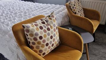 A hotel room with a bed, two armchairs with polka dot cushions, a lamp, and a window with curtains.