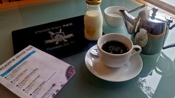 Uma mesa de café da manhã com um cardápio, uma xícara de café, um garrafão de leite e um bule de prata.