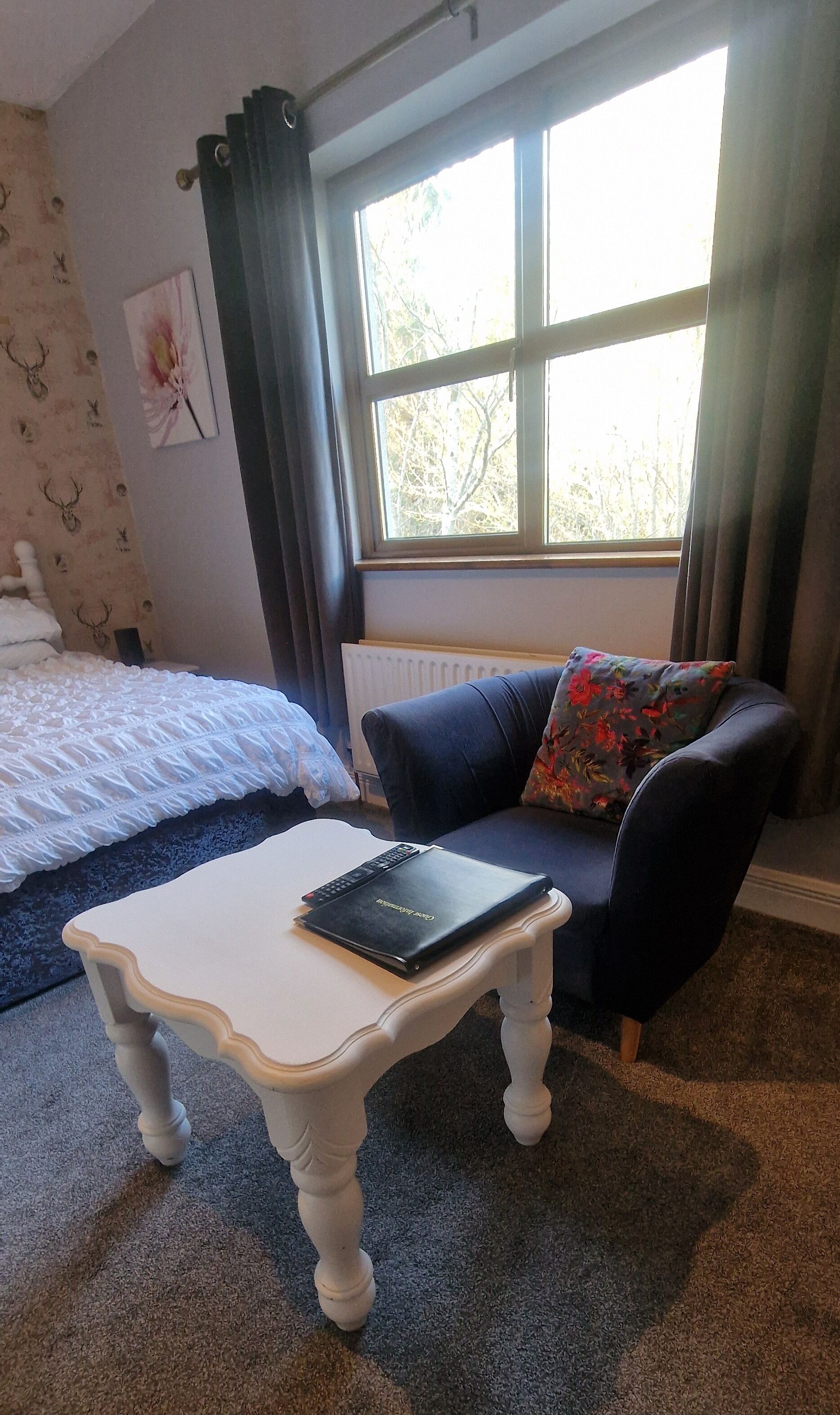 Um quarto com uma cama, um sofá, uma mesinha com um laptop e uma janela com cortinas.