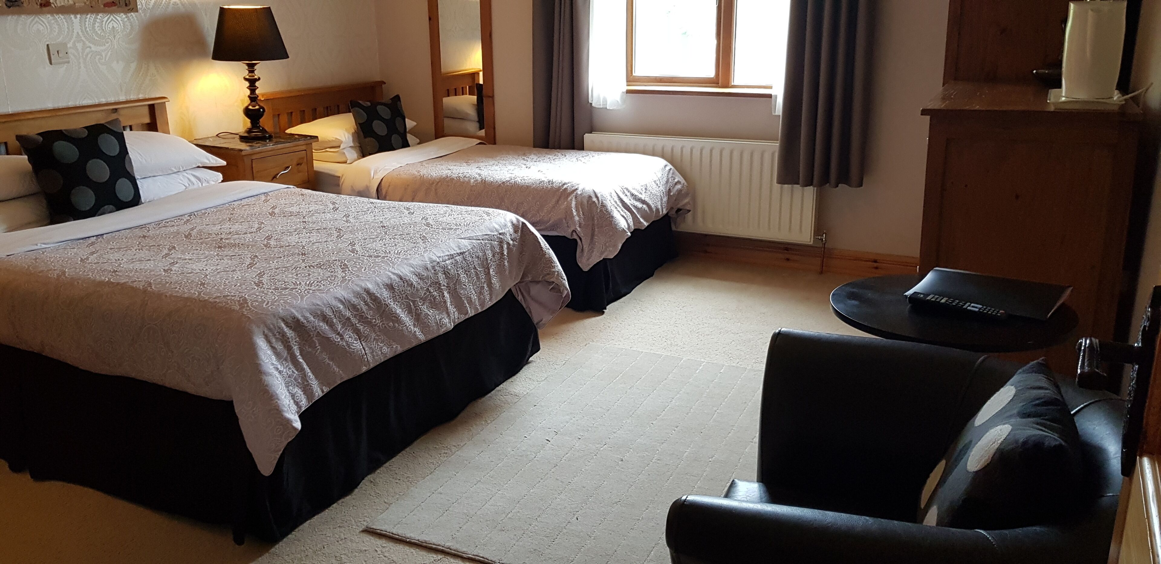 A hotel room with two beds, a desk, a chair, a lamp, and a window with curtains.