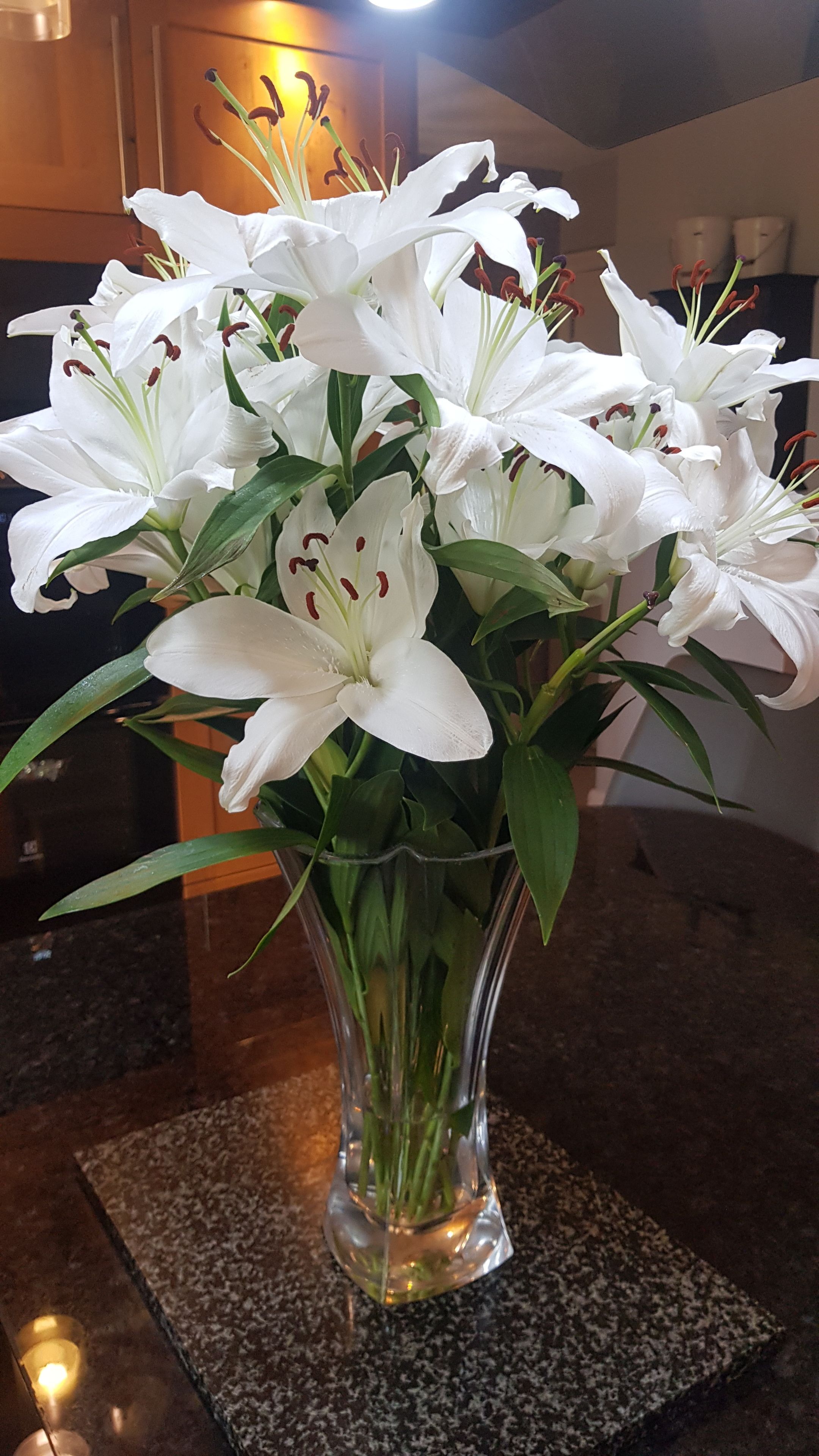 A clear glass vase with white lilies on a granite countertop.