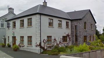 A two-story building with a white facade and stone accents, featuring multiple windows and a small garden area in front.