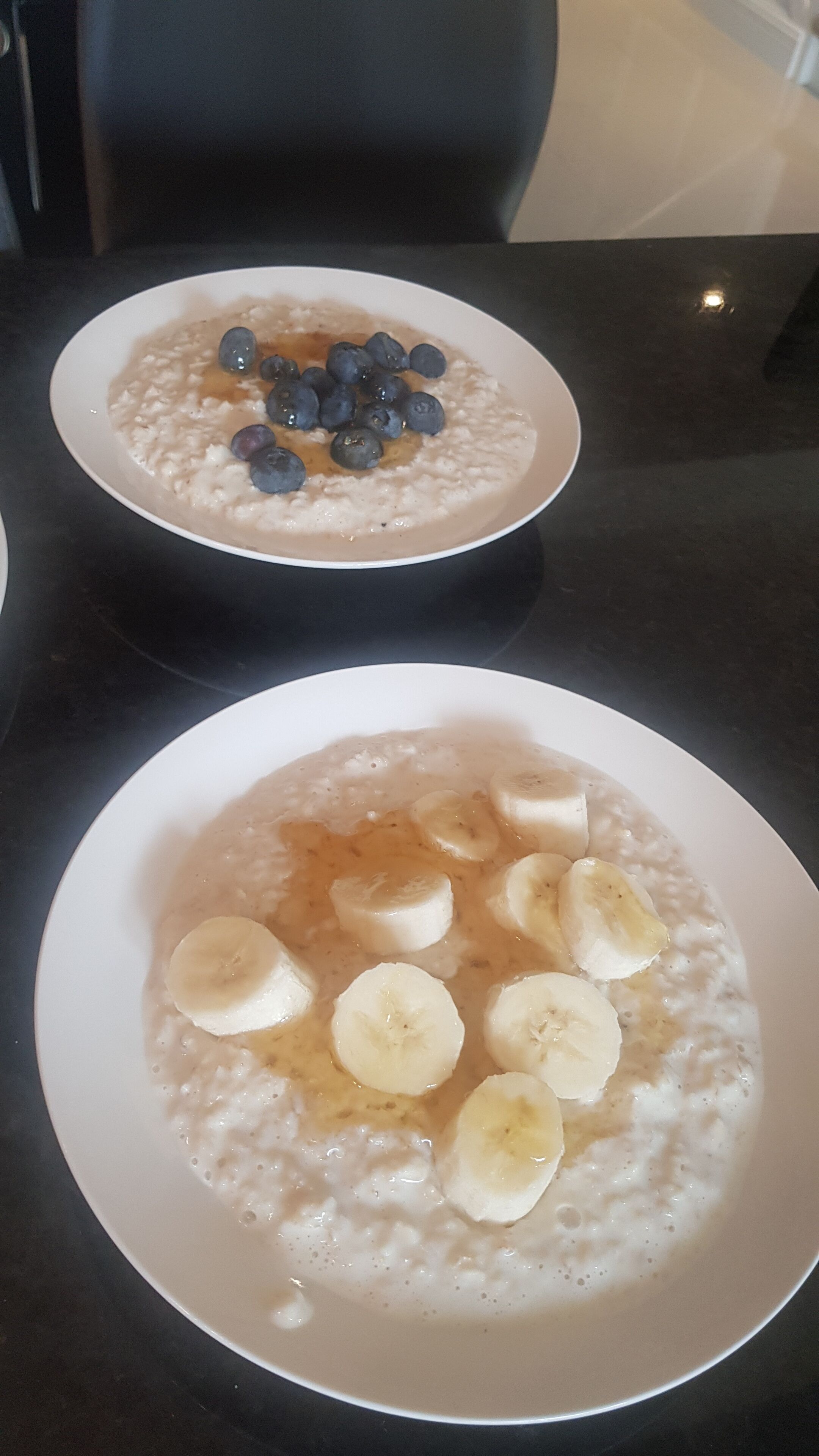 Dos tazones de avena con arándanos y rodajas de plátano sobre una mesa.