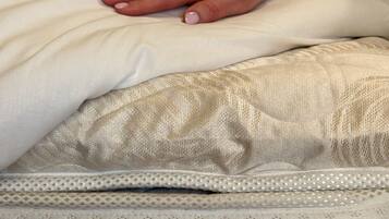 A hand resting on a bed with a patterned pillow and a quilted mattress.
