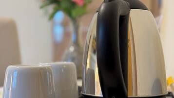 Une machine à café avec deux tasses posées sur un plateau, placée sur une table. En arrière-plan, on aperçoit un vase rempli de fleurs roses.