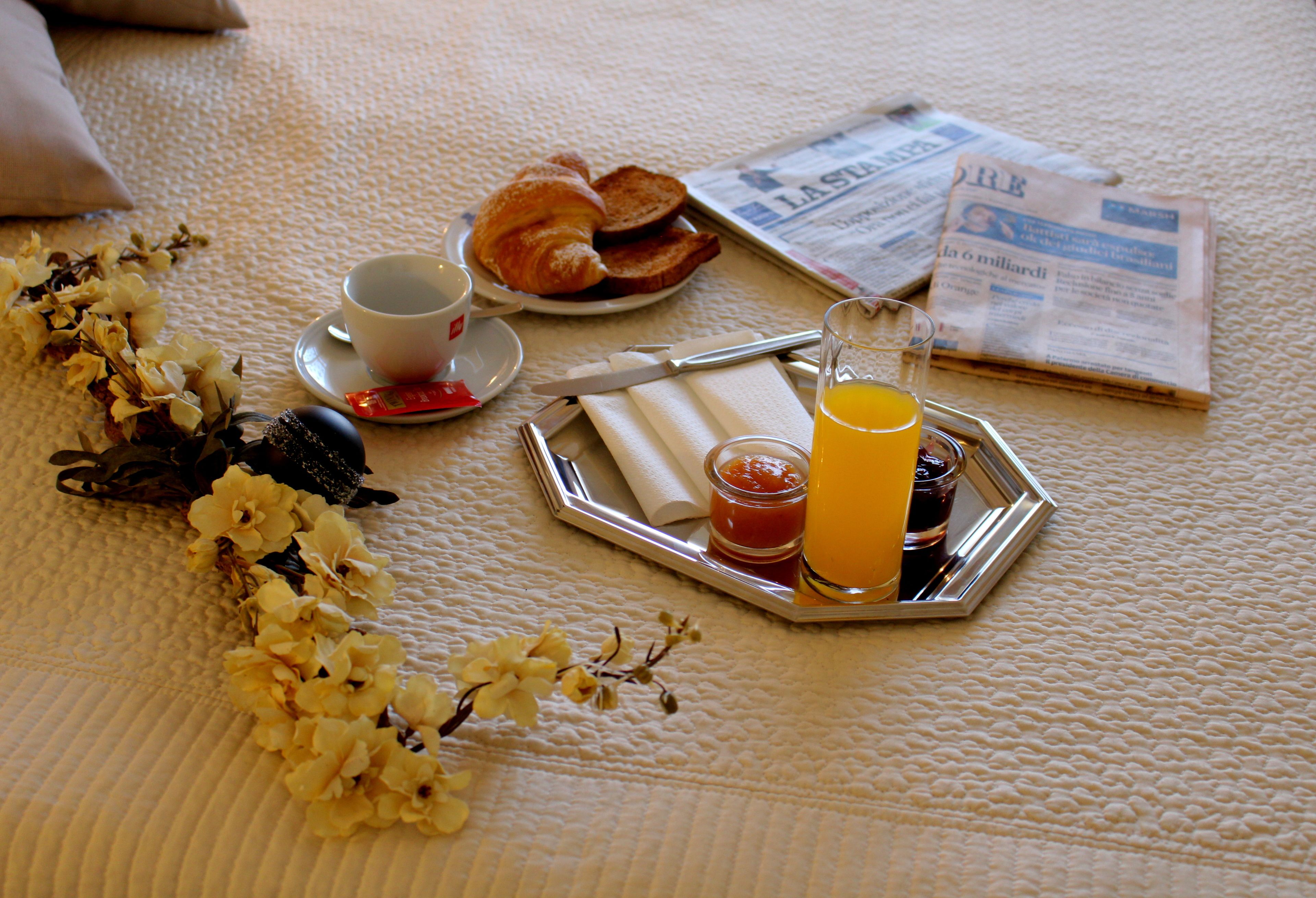 Bandeja de desayuno con cruasanes, una taza de café, un vaso de jugo de naranja y un periódico sobre una colcha texturizada.