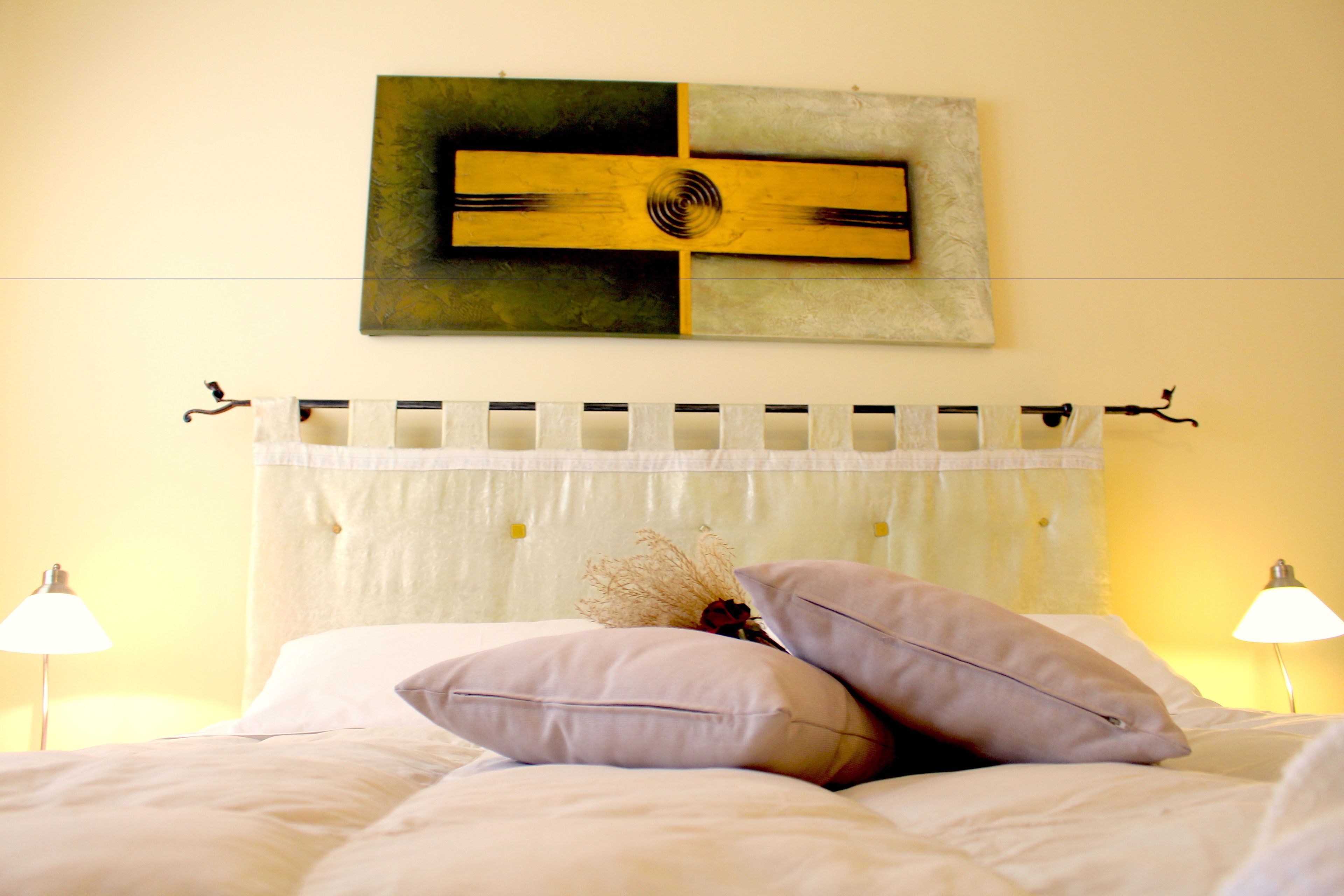 Un letto rifatto con cuscini, una testiera decorata e due abat-jour.