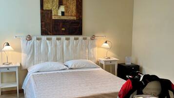 A neatly arranged hotel room with a bed, bedside lamps, a wall art piece, and a table with a suitcase and a helmet.