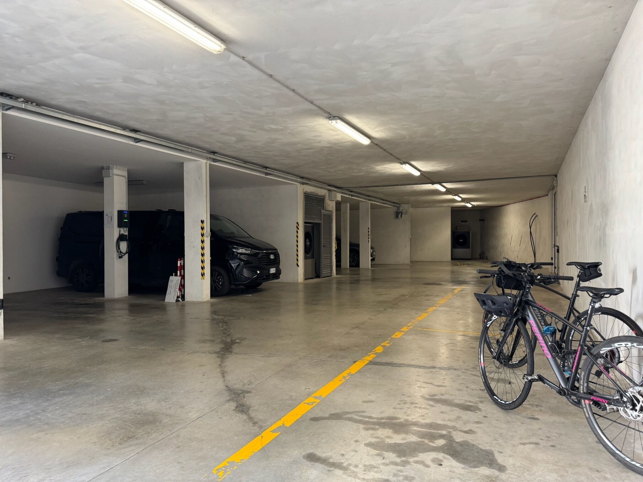 Un aparcamiento con suelo de hormigón, líneas amarillas y una bicicleta estacionada junto a la pared.