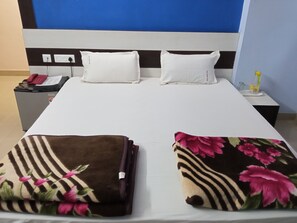 A hotel room with a bed, two pillows, a nightstand with a phone, a lamp, and a small table with a bottle. - Hotel Viraat Inn (Gaya)