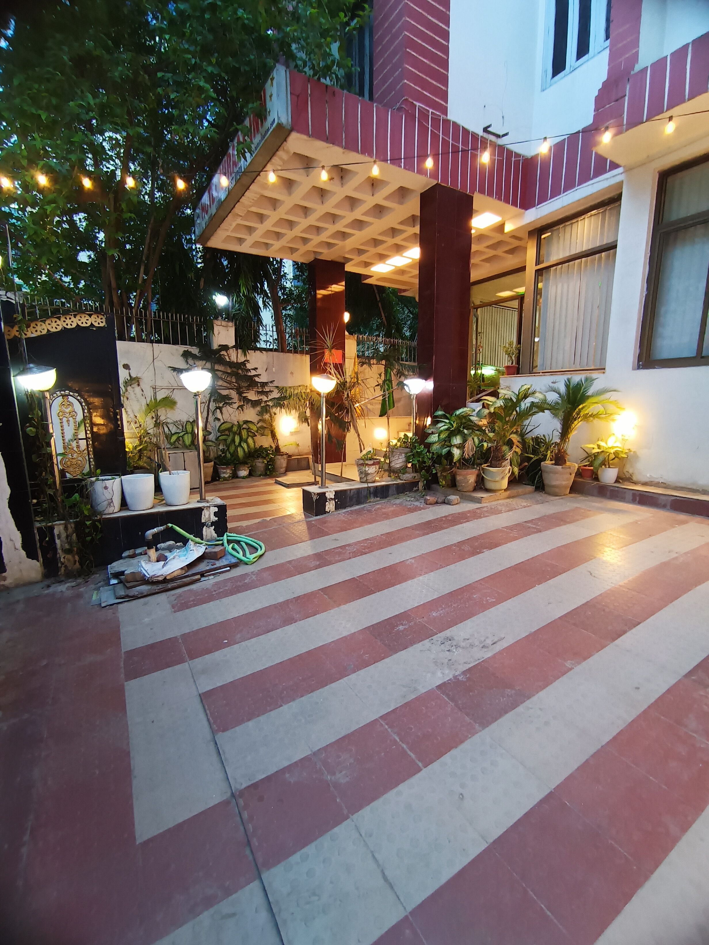 Un patio con plantas en macetas, suelo de baldosas y luces colgantes.