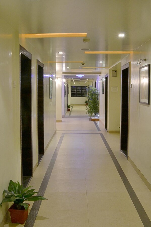 A long, narrow hallway with doors on both sides, potted plants, and recessed lighting.