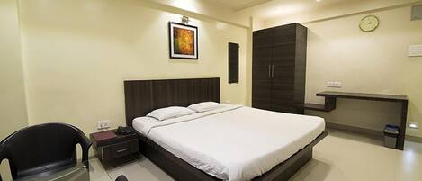 Una habitación de hotel con cama, escritorio, silla, armario y ventilador de techo.