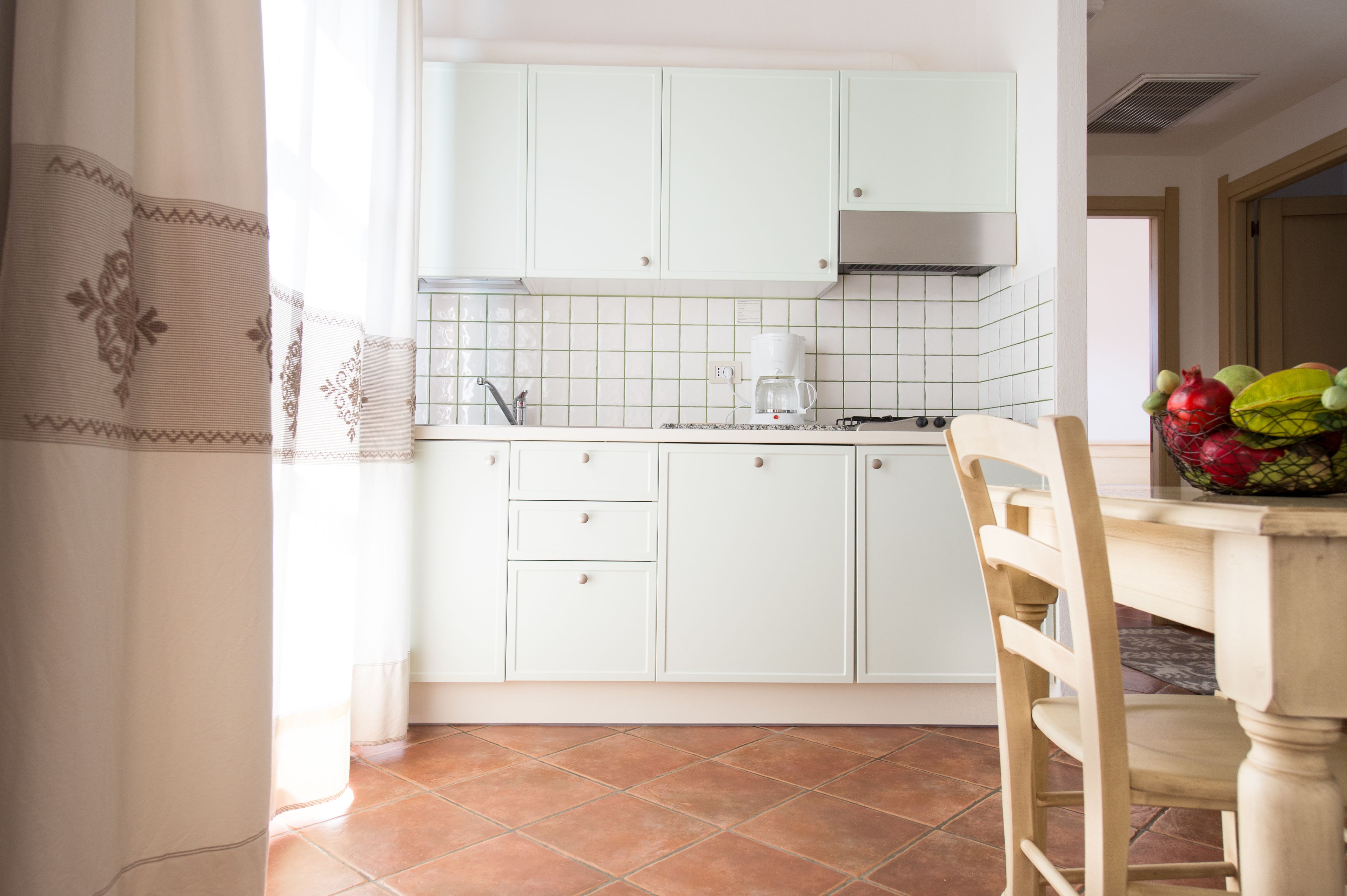 Una cocina con armarios blancos, una cafetera y un frutero en la encimera.