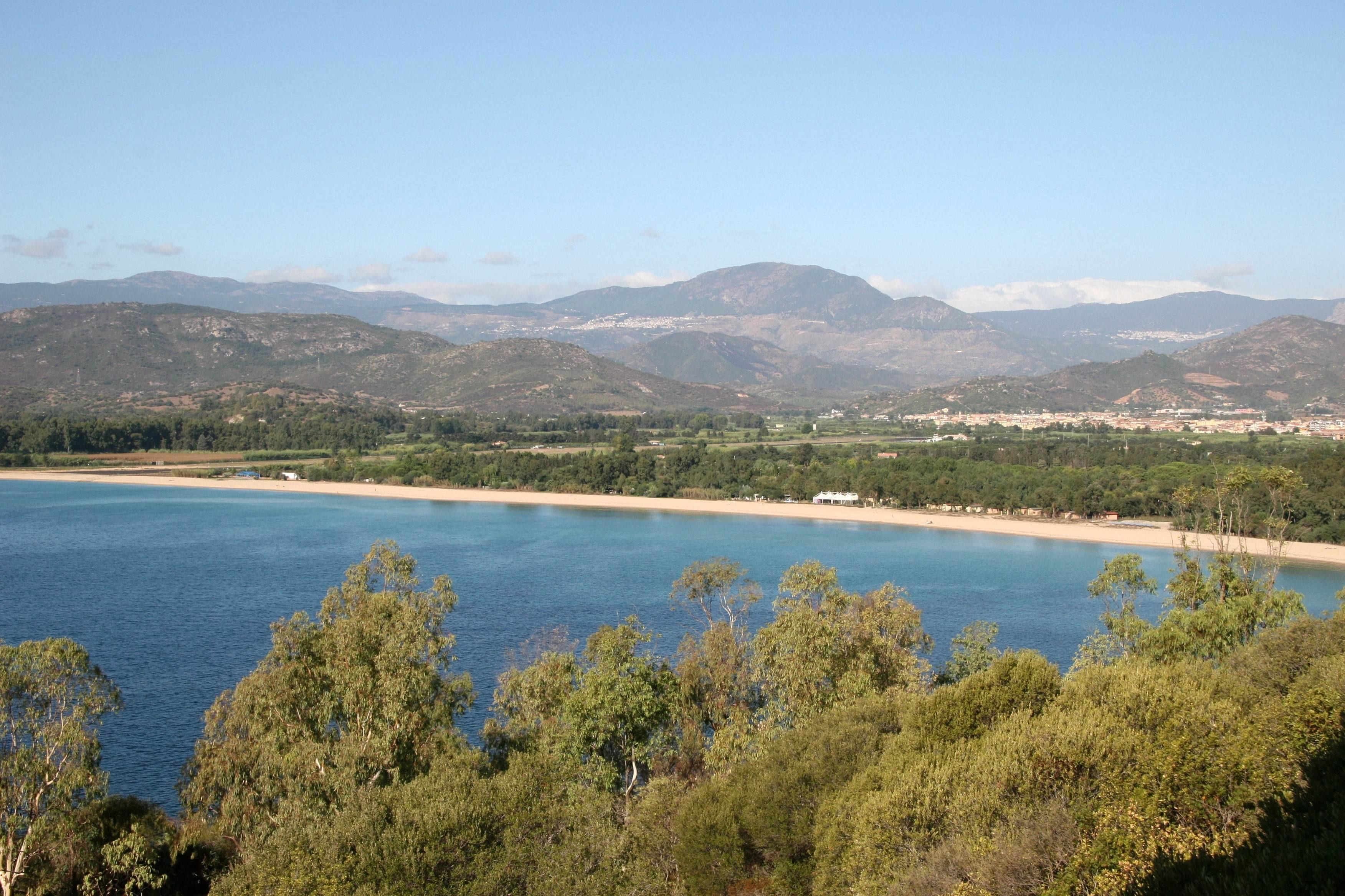 Eine Küstenlandschaft mit Strand, klarem blauen Wasser und Bergen im Hintergrund.