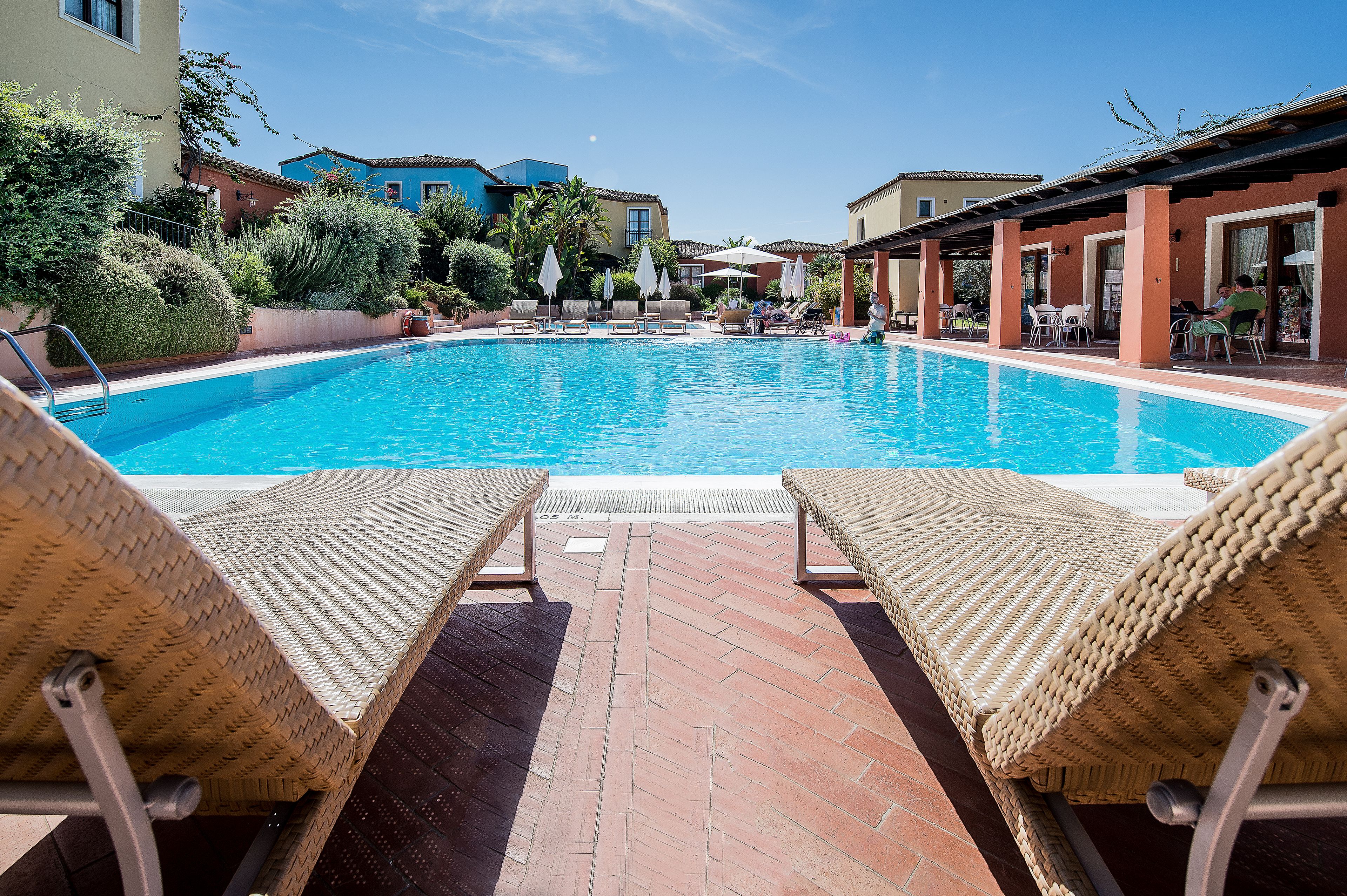 Piscina com espreguiçadeiras e guarda-sóis, cercada por edifícios com telhado ladrilhado.