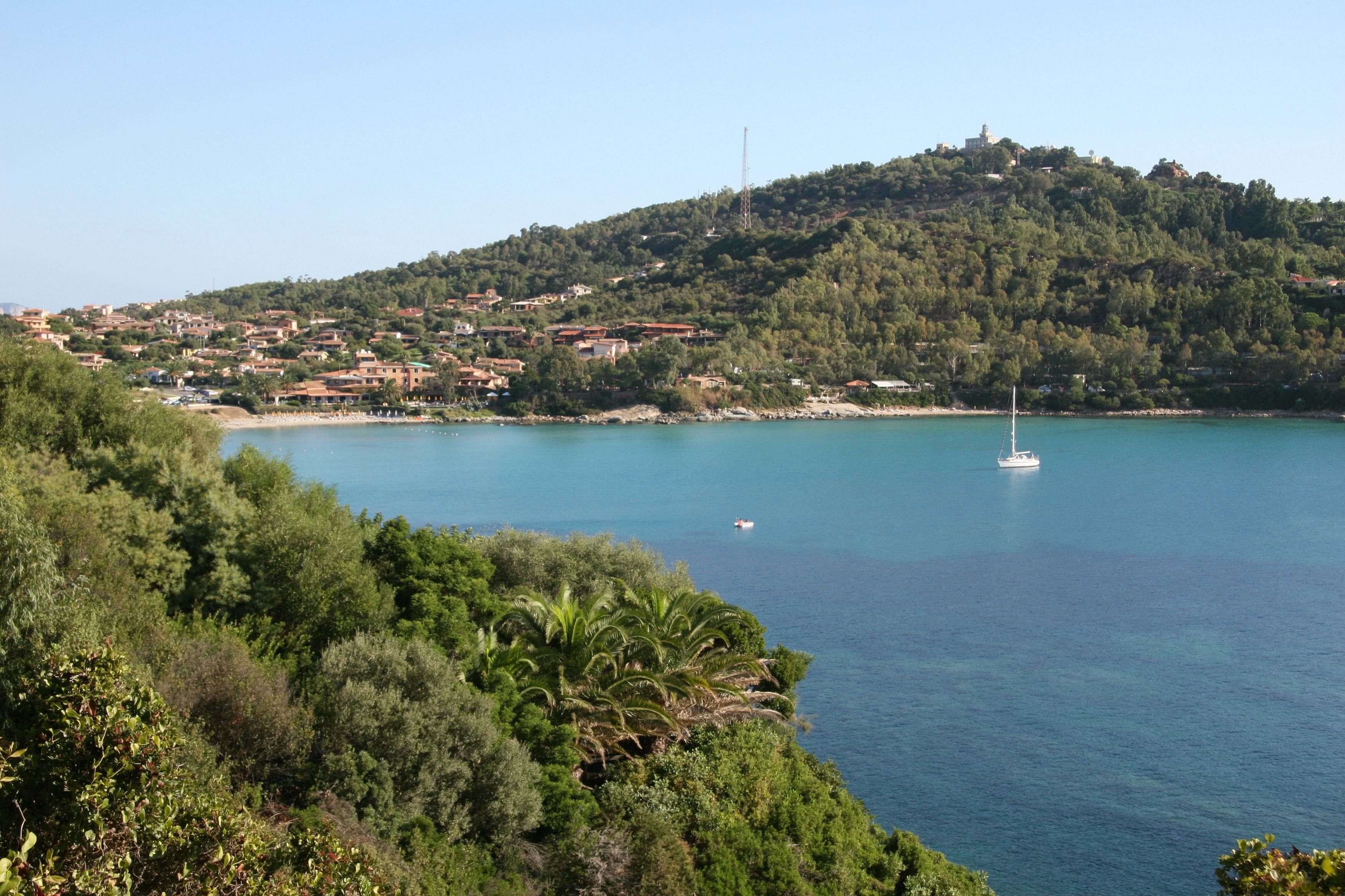 A coastal town with a hilltop view, a clear blue sea, and a sailboat.