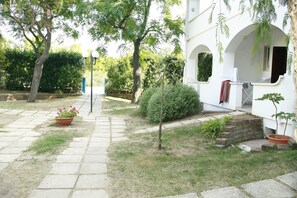 A courtyard with a stone pathway, a small tree, and a potted plant with flowers. - Park Hotel Valle Clavia (Peschici)