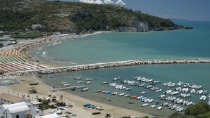 Una zona costera con playa, puerto deportivo y edificios.