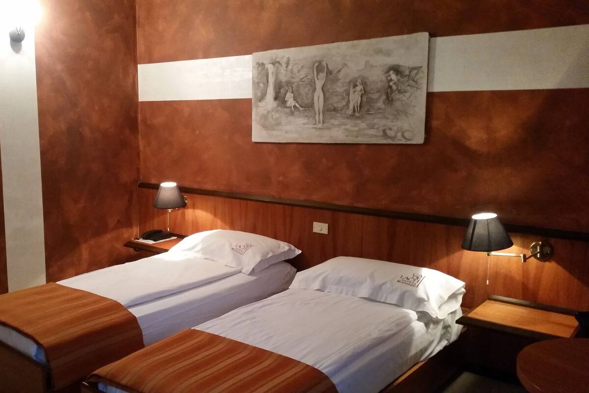 A hotel room with two beds, a painting on the wall, and bedside lamps.