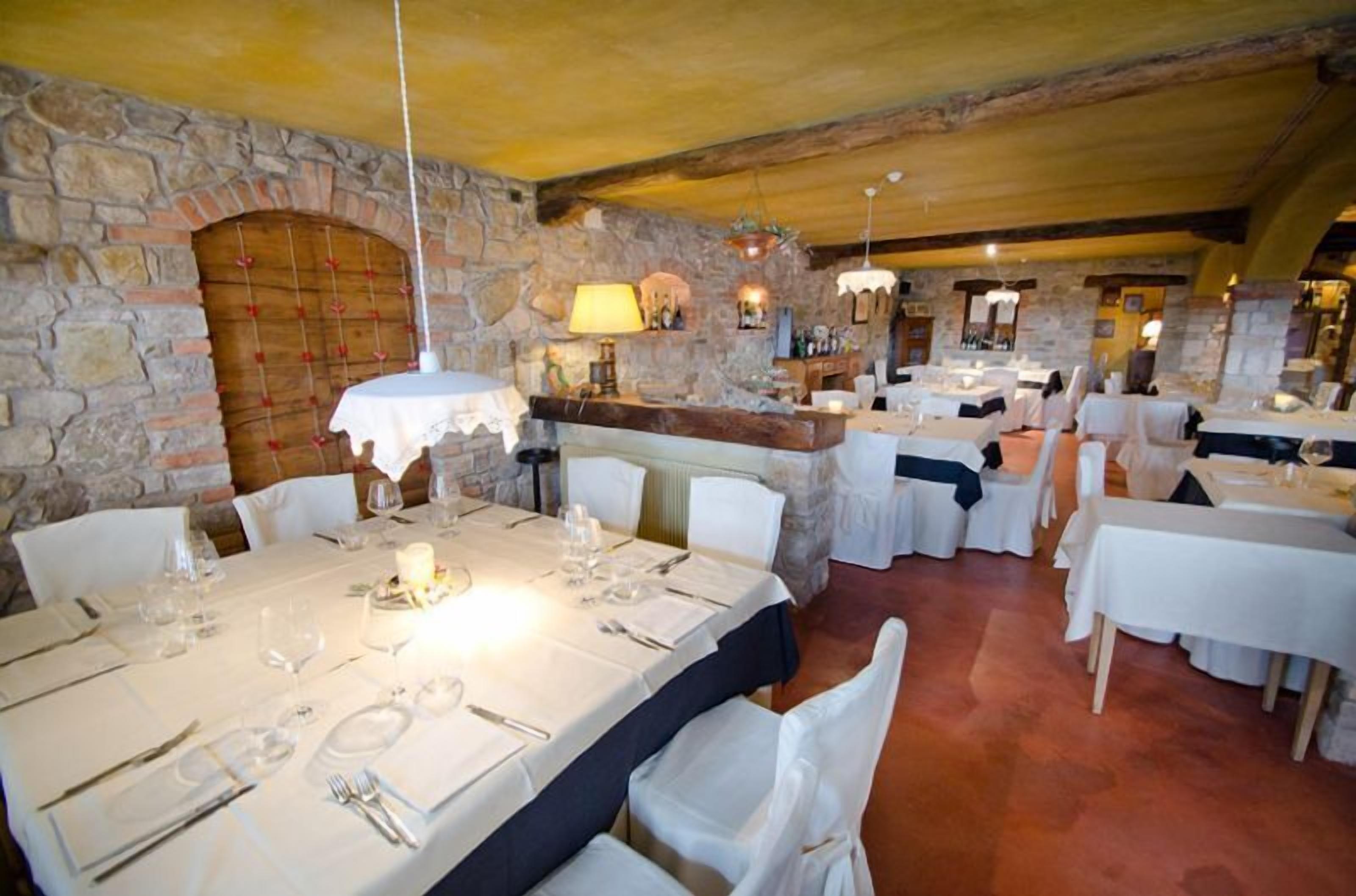 Un restaurante con paredes de piedra, manteles blancos y mesas iluminadas con velas.