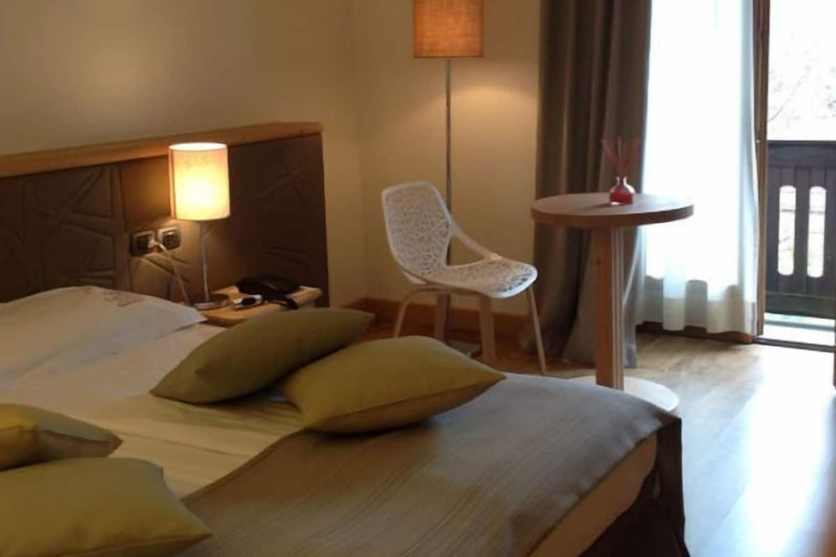 A hotel room with a large bed, a bedside lamp, a chair, and a small table.