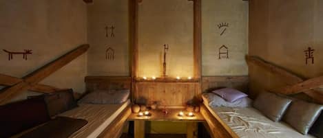 A cozy, rustic room with wooden beams, a central table with candles, and simple bed arrangements.