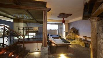 Un interior rústico con una escalera de piedra, una mesa de billar y una pared de piedra con una escultura de oso.