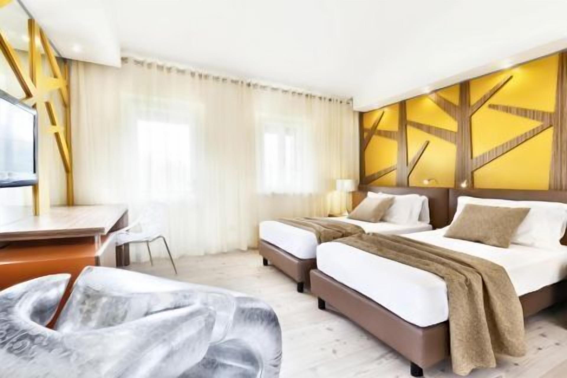 Una camera d'albergo con due letti, una scrivania e una sedia.