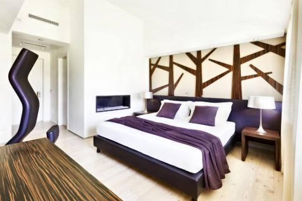 A modern hotel room with a large bed, a TV mounted on the wall, and a unique wooden headboard design.